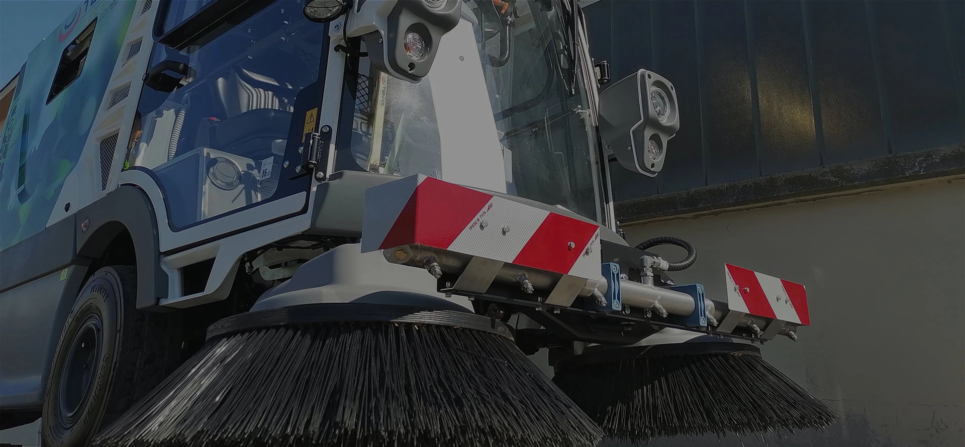 Close-up of a Tenax electric street sweeper with large rotating brushes.