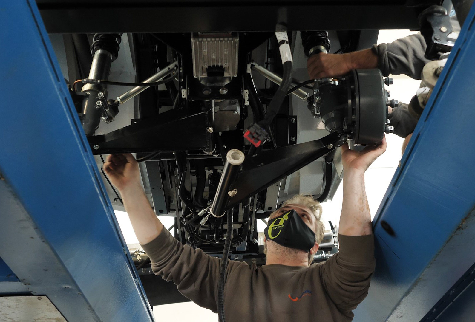 A technician working under a Tenax electric street sweeper, inspecting and adjusting mechanical components.